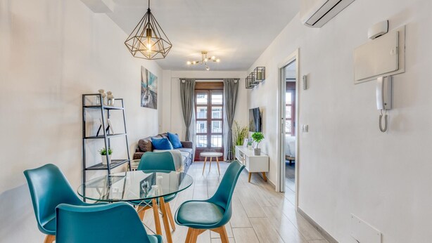 Un salon moderne avec une table à manger en verre, des chaises de couleur turquoise, un canapé et une suspension au design géométrique.