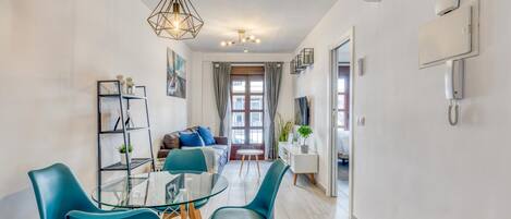 Un salon moderne avec une table à manger en verre, des chaises de couleur turquoise, un canapé et une suspension au design géométrique.