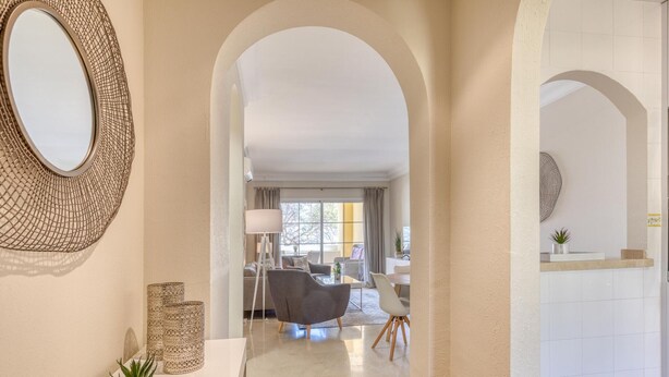 A modern interior with a hallway leading to a dining area. There is a round mirror on the left, a potted plant, and a lamp. The dining area has a table and chairs. - Beautiful 2-Bedroom Apartment in Estepona with Pool and Terrace (Estepona)