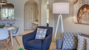 A modern living room with a dark blue armchair, a white floor lamp, and a patterned throw pillow. - Beautiful 2-Bedroom Apartment in Estepona with Pool and Terrace (Estepona)