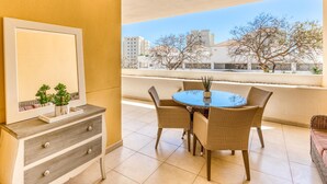 A balcony with a round table and wicker chairs, a dresser with drawers, and a framed picture on the wall. - Beautiful 2-Bedroom Apartment in Estepona with Pool and Terrace (Estepona)
