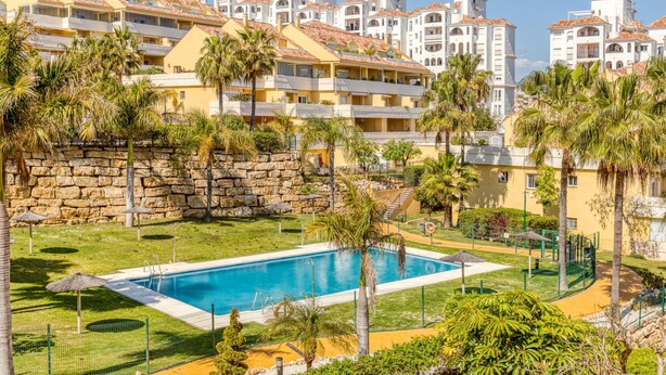 A resort with a swimming pool surrounded by palm trees and a stone wall. - Modern apartment in Estepona, ground floor with terrace and pool, close to port and beach (Estepona)