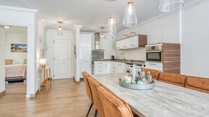 A modern kitchen with white cabinets, a wooden countertop, and a dining area with a marble table and leather chairs. - Modern apartment in Estepona, ground floor with terrace and pool, close to port and beach (Estepona)