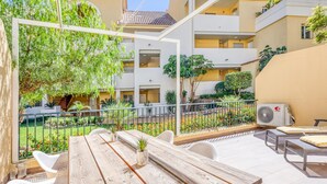 An outdoor patio with a wooden table and chairs, surrounded by a garden with various plants and flowers. - Modern apartment in Estepona, ground floor with terrace and pool, close to port and beach (Estepona)