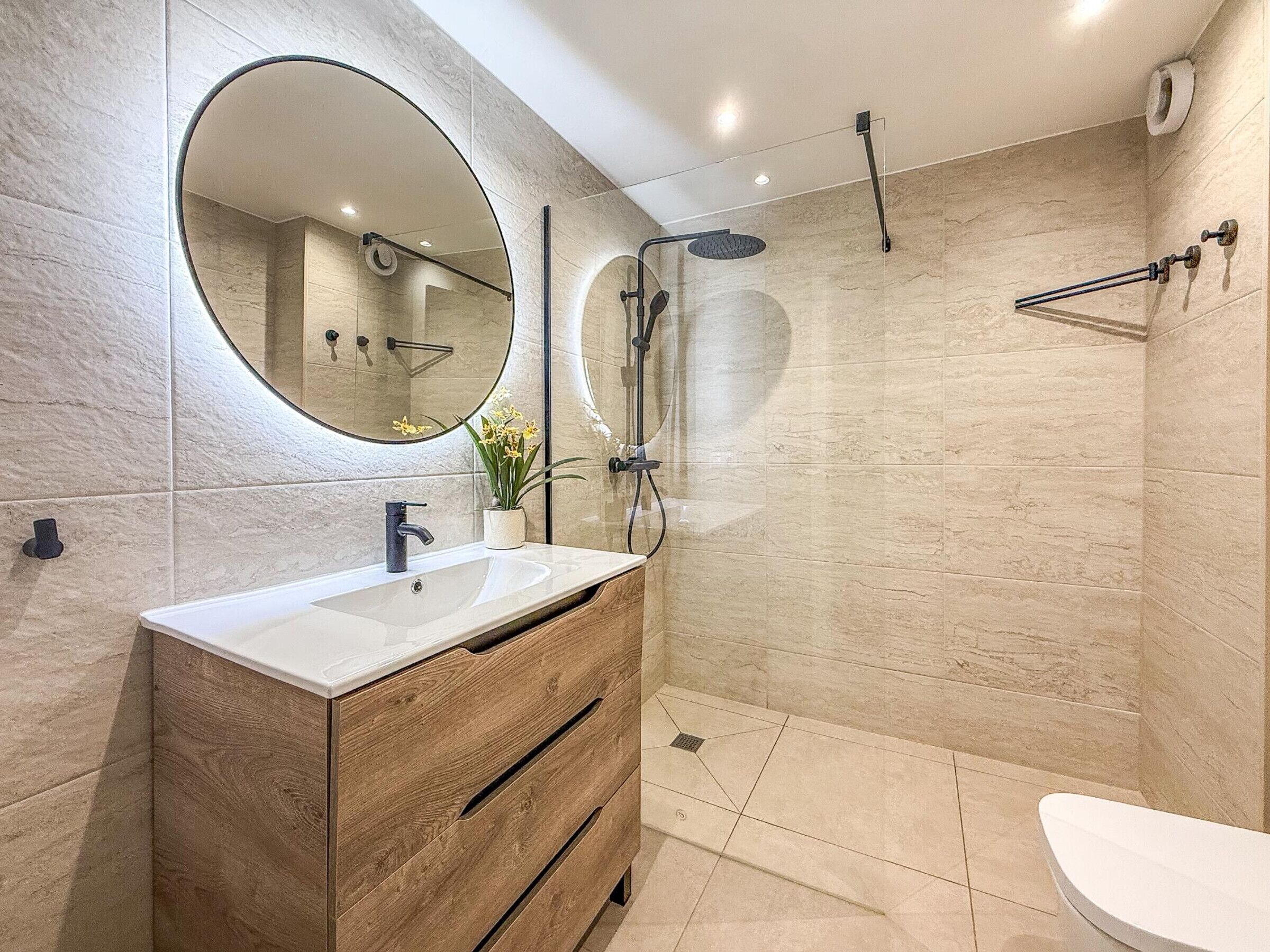 A modern bathroom with a wooden vanity, a large mirror, and a walk-in shower.