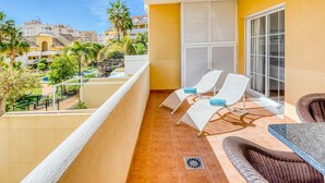 A balcony with two white lounge chairs, a wicker sofa, and a view of a residential area with palm trees and buildings. - Bright 2-Bed Apartment in Estepona's Peaceful Puerto Alto with Pools and Terrace (Estepona)
