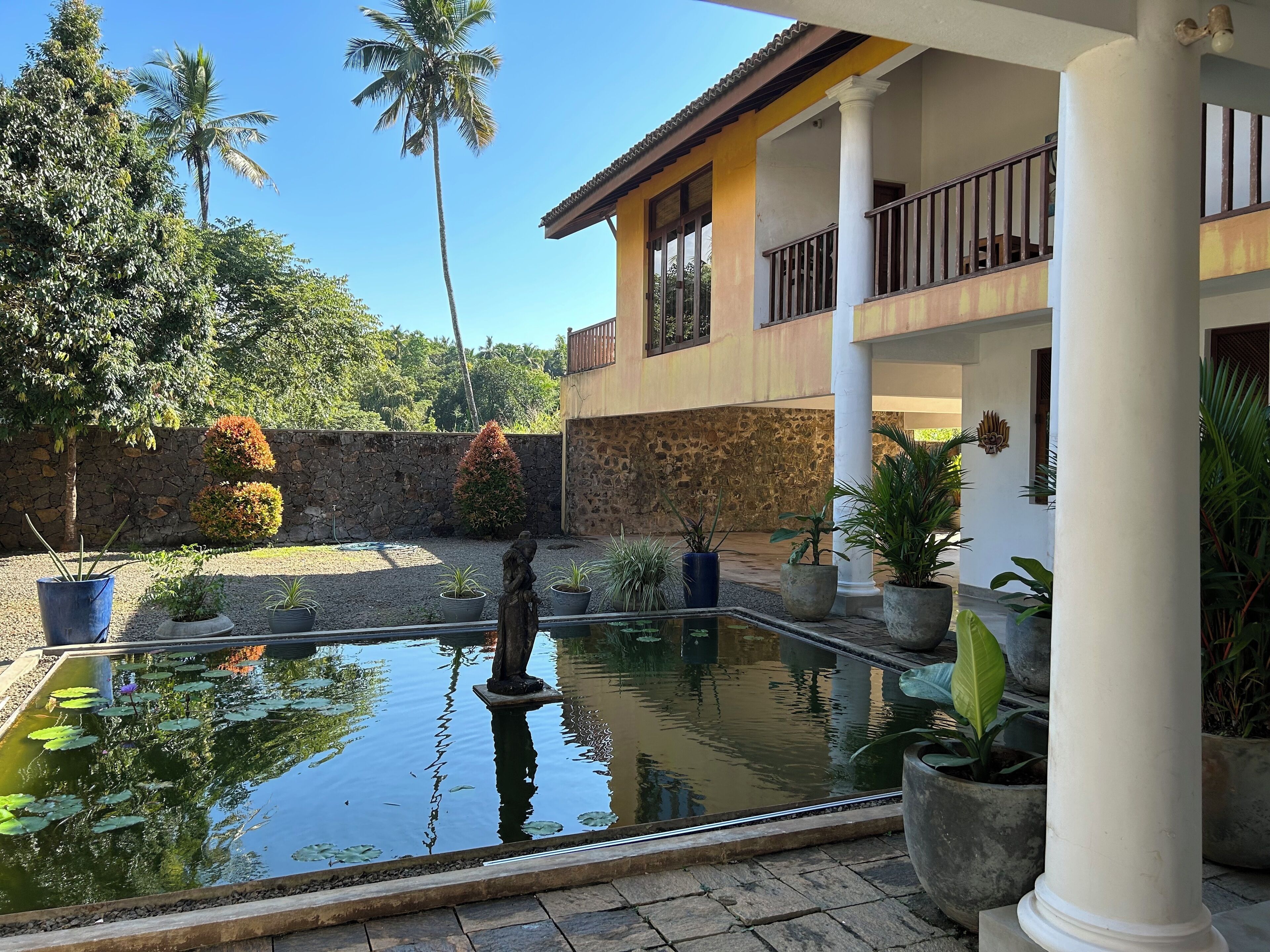 Un patio con piscina, plantas en macetas y un muro de piedra.