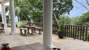 Une table dressée pour le petit-déjeuner, avec des chaises, et en toile de fond, une vue sur une végétation luxuriante et une piscine.