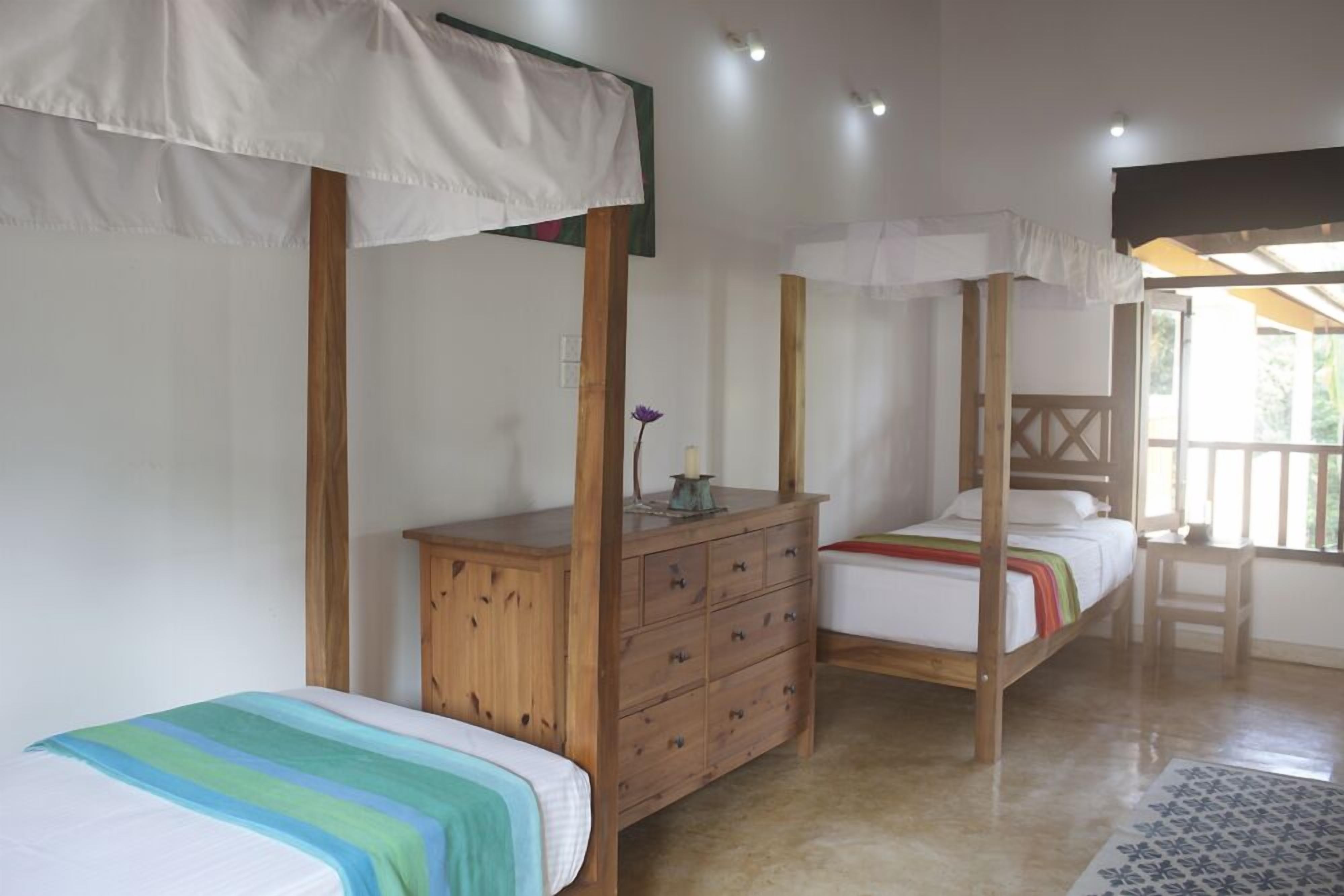 A bedroom with two single beds, a wooden dresser, and a canopy bed.