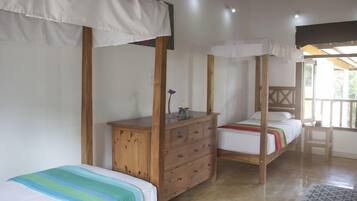 Quarto com duas camas de solteiro, cômoda de madeira e uma cama com dossel.