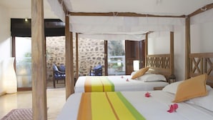 Une chambre avec deux lits, un mur en pierre et une vue sur l’extérieur.