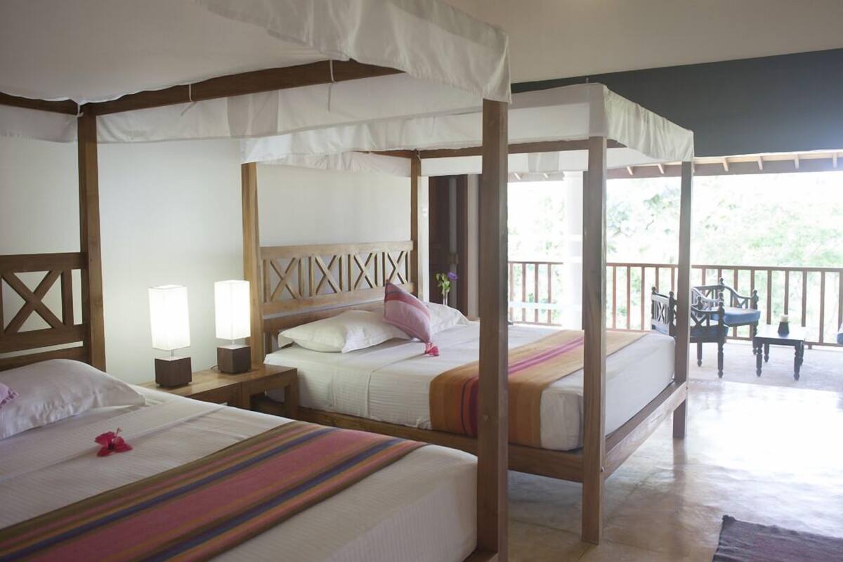 A room with four beds, each with a canopy, wooden headboards, and bedside lamps.