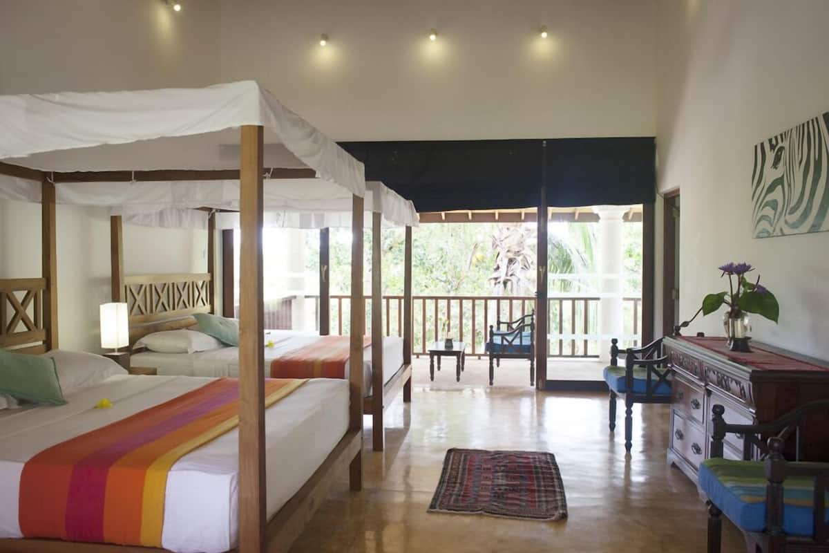 A four-poster bed with a canopy, a wooden dresser, and a balcony with a view of greenery.