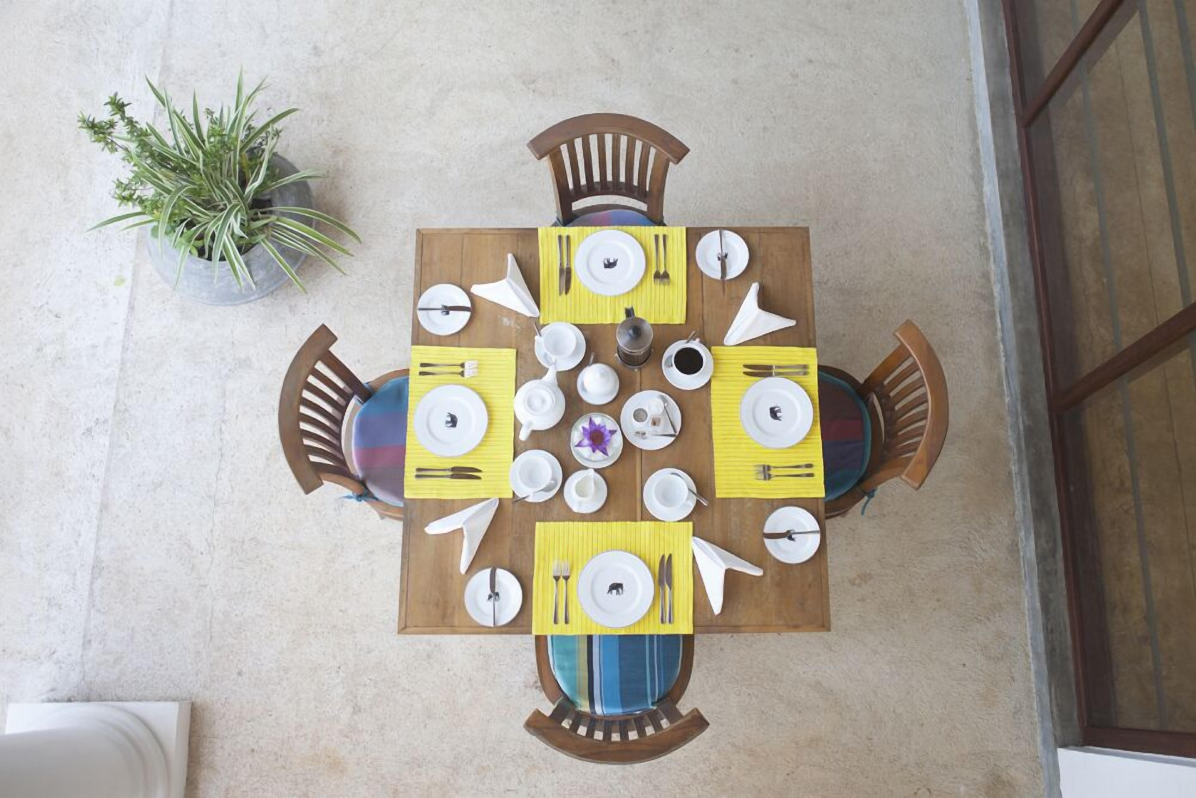 A dining table set for four with yellow placemats, white plates, and cutlery.