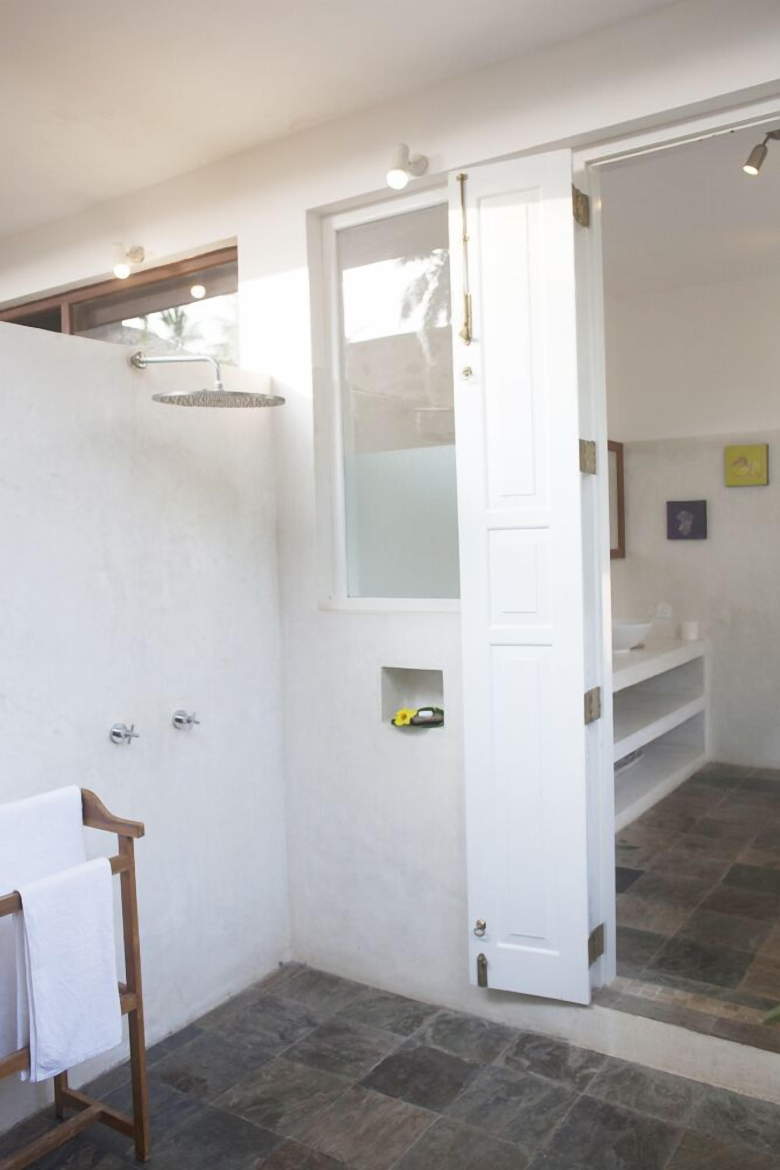 A bathroom with a shower, a towel rack, and a door leading to another room.