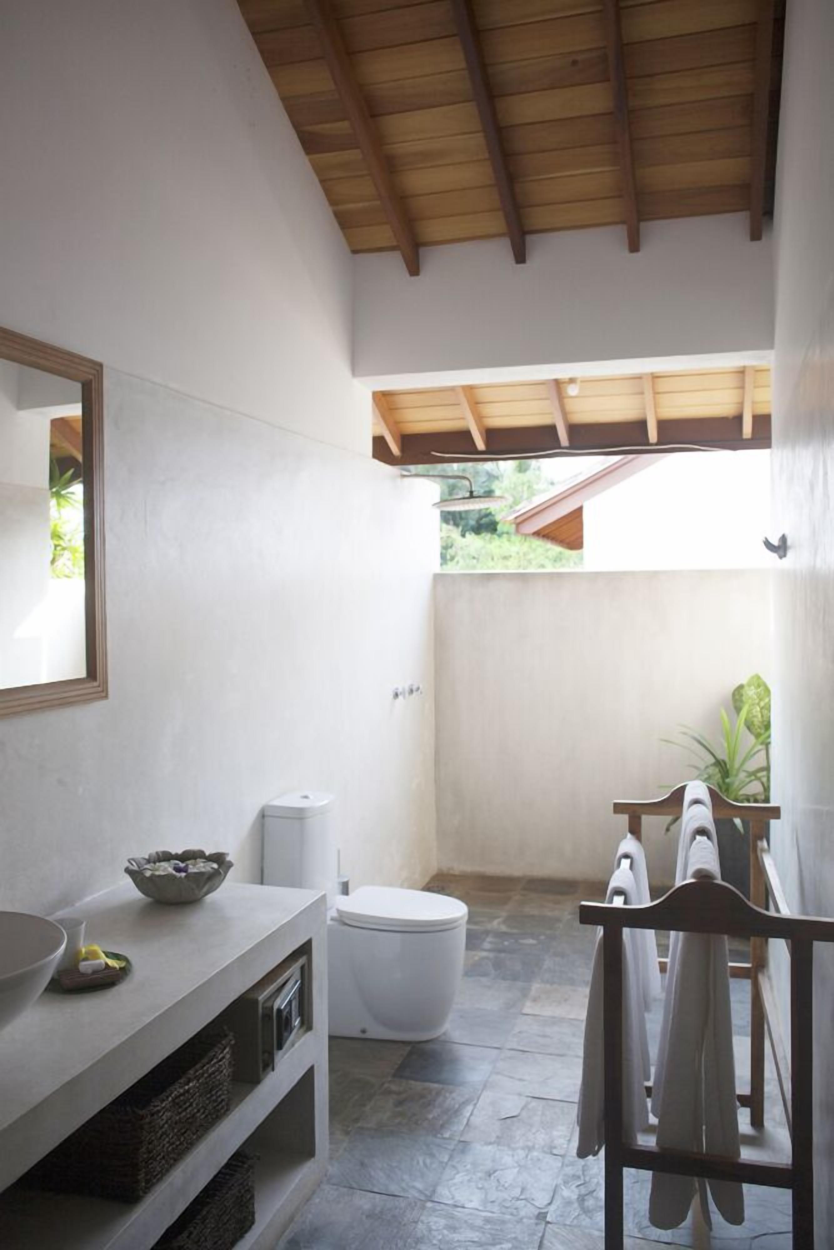 Un baño con un lavamanos blanco, un espejo, un inodoro blanco y una zona de ducha.