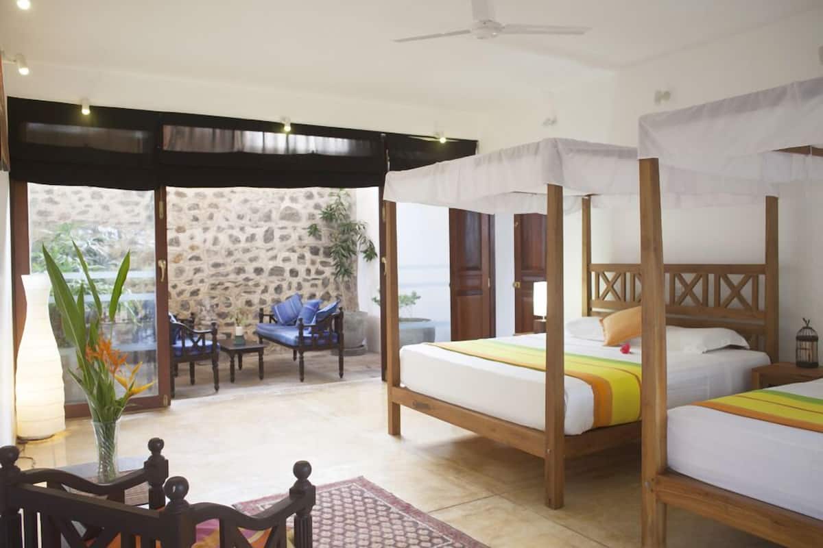 A room with two wooden beds, a stone wall, a potted plant, and a seating area with chairs and a table.