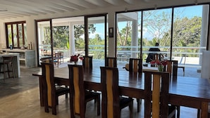 Un vaste espace à manger avec une grande table et des chaises, de grandes fenêtres donnant sur l’extérieur et un ventilateur de plafond.