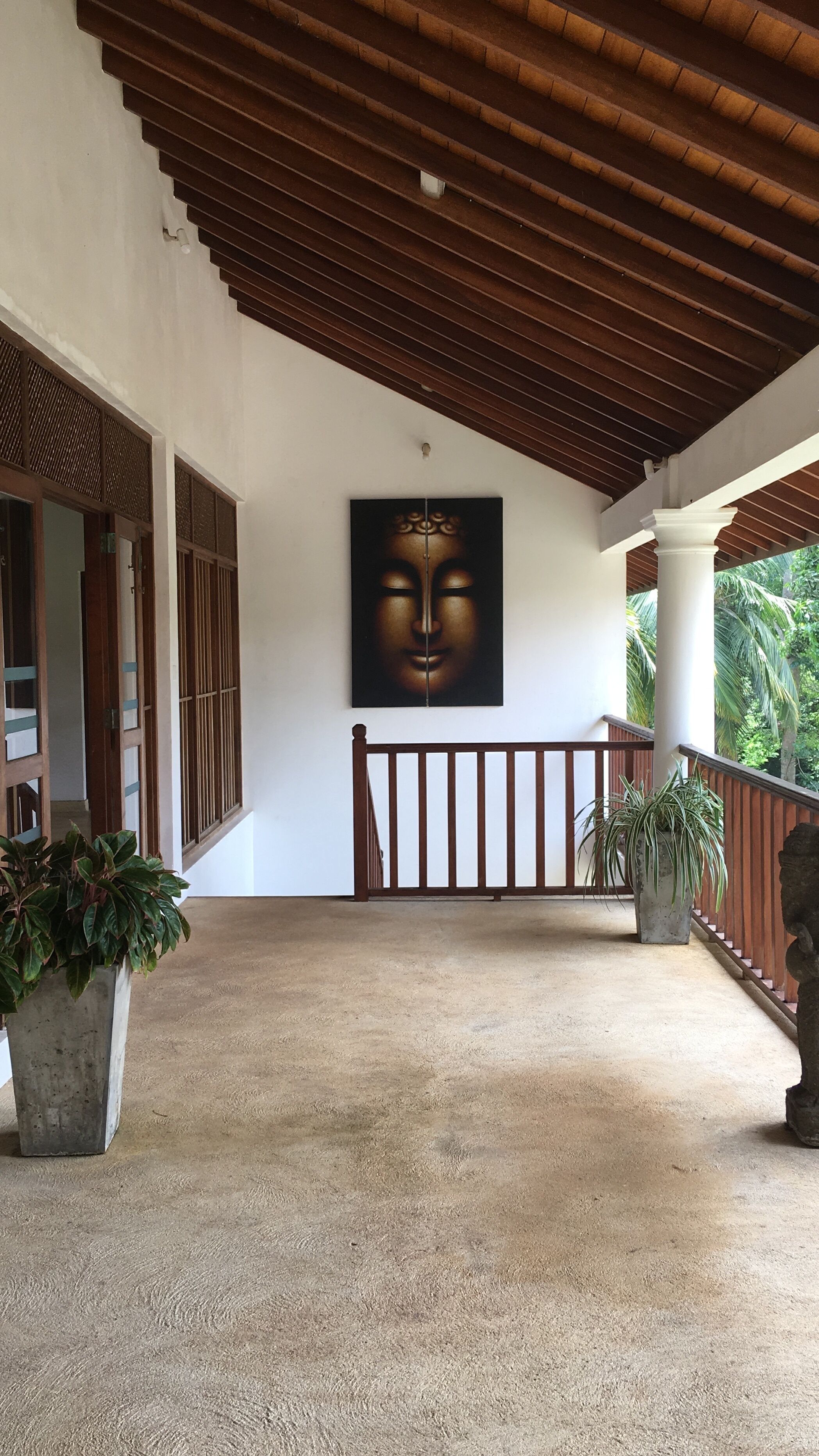 A covered outdoor area with a wooden ceiling, a large painting on the wall, and potted plants.