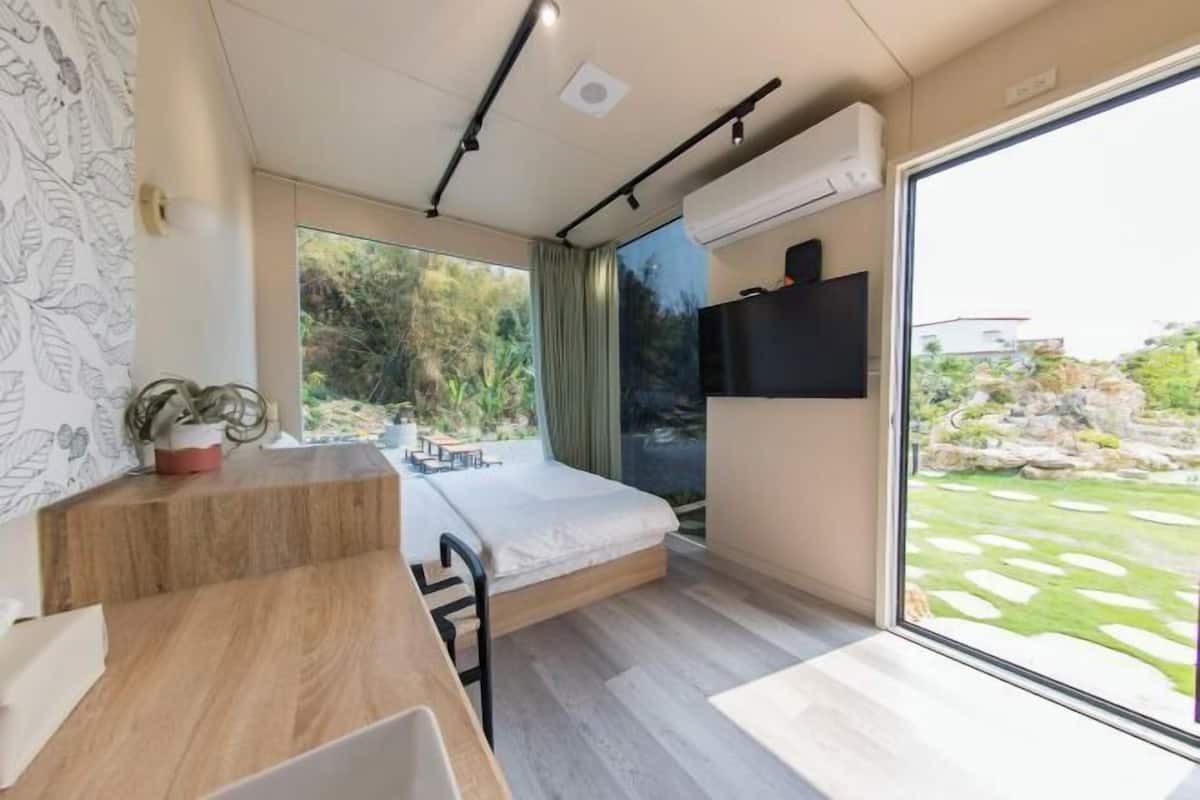 Een moderne kamer met een bed, een bureau en een groot raam met uitzicht op een tuin.