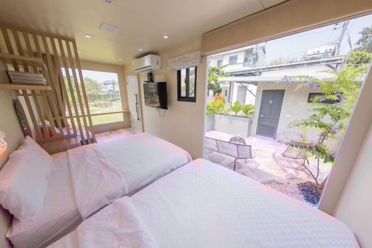 A bedroom with two beds, a TV, and a view of the outside courtyard.