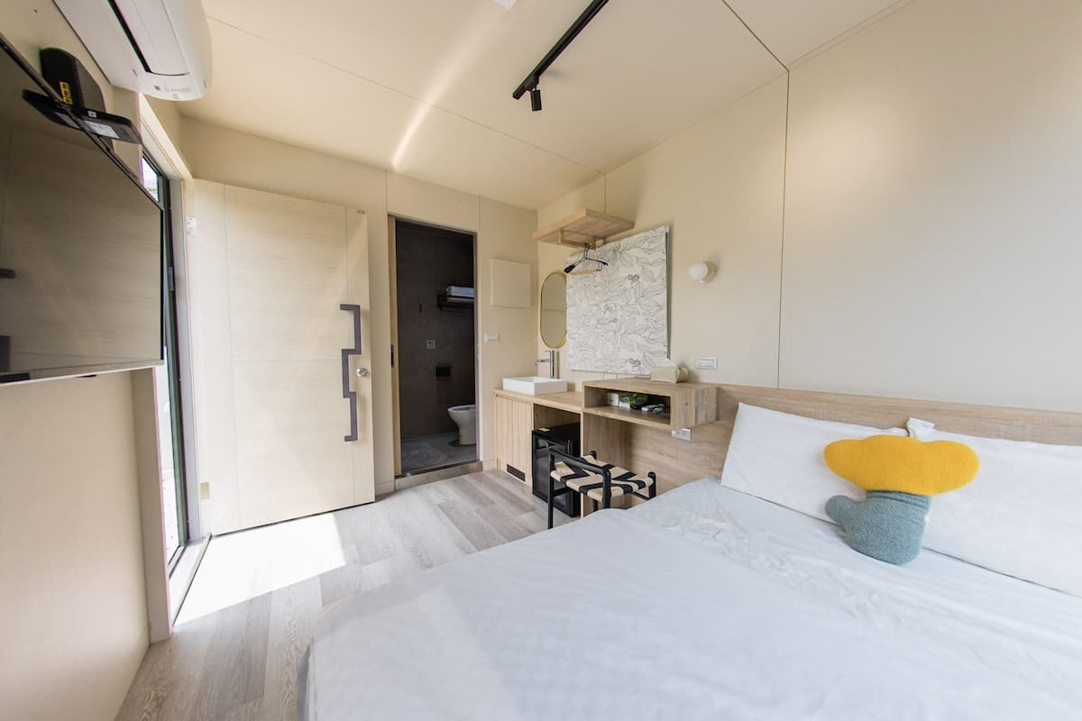 Een moderne hotelkamer met een bed, een bureau, een spiegel en een badkamer die door een open deur zichtbaar is.