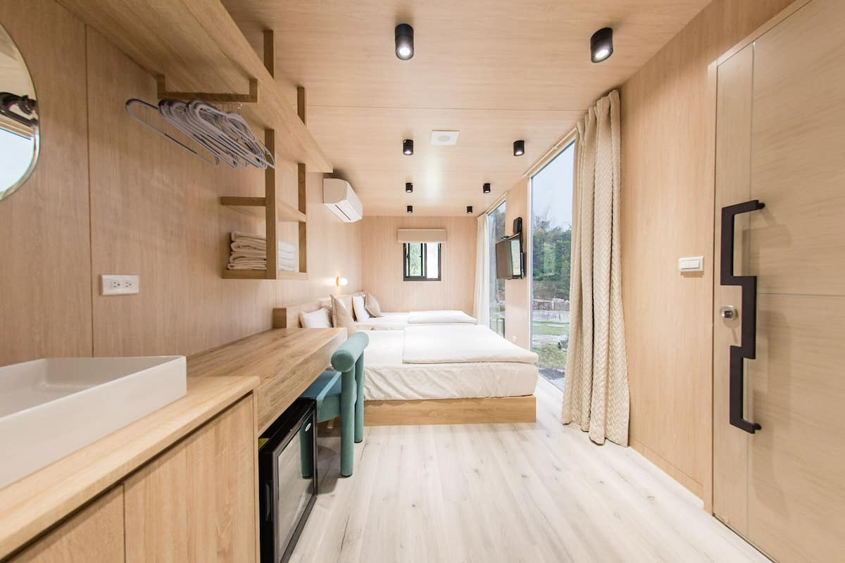 Een moderne slaapkamer met een houten vloer, een groot bed, een nachtkastje, een spiegel en een raam met gordijnen.