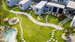 A modern residential complex with a central courtyard featuring a circular stone pathway, outdoor seating, and a small inflatable play area.