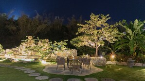 An outdoor patio with a stone table and chairs, surrounded by a well-maintained lawn and decorative rocks.