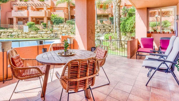 A sunlit outdoor patio with a round table, wicker chairs, and a pool view.