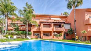 A swimming pool with a clear blue water surface, surrounded by a building with a terracotta facade and balconies.