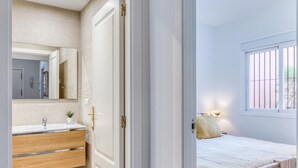 A bedroom with a bed, a window, and a bathroom with a sink and mirror.
