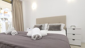 A neatly made bed with rolled towels, a headboard, and a bedside table with a power outlet.