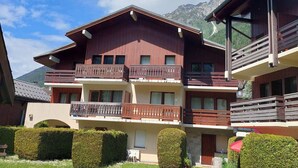 A multi-story chalet with balconies, a covered outdoor seating area, and a mountain backdrop.