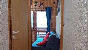 A room with a wooden door, a grey sofa with red cushions, and a window with blue curtains.
