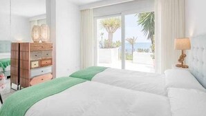 A hotel room with a large bed, a wooden dresser, a lamp, and a view of the sea. - Luxury beachfront apartment with pool, gardens, tennis courts and restaurant in Estepona (Estepona)