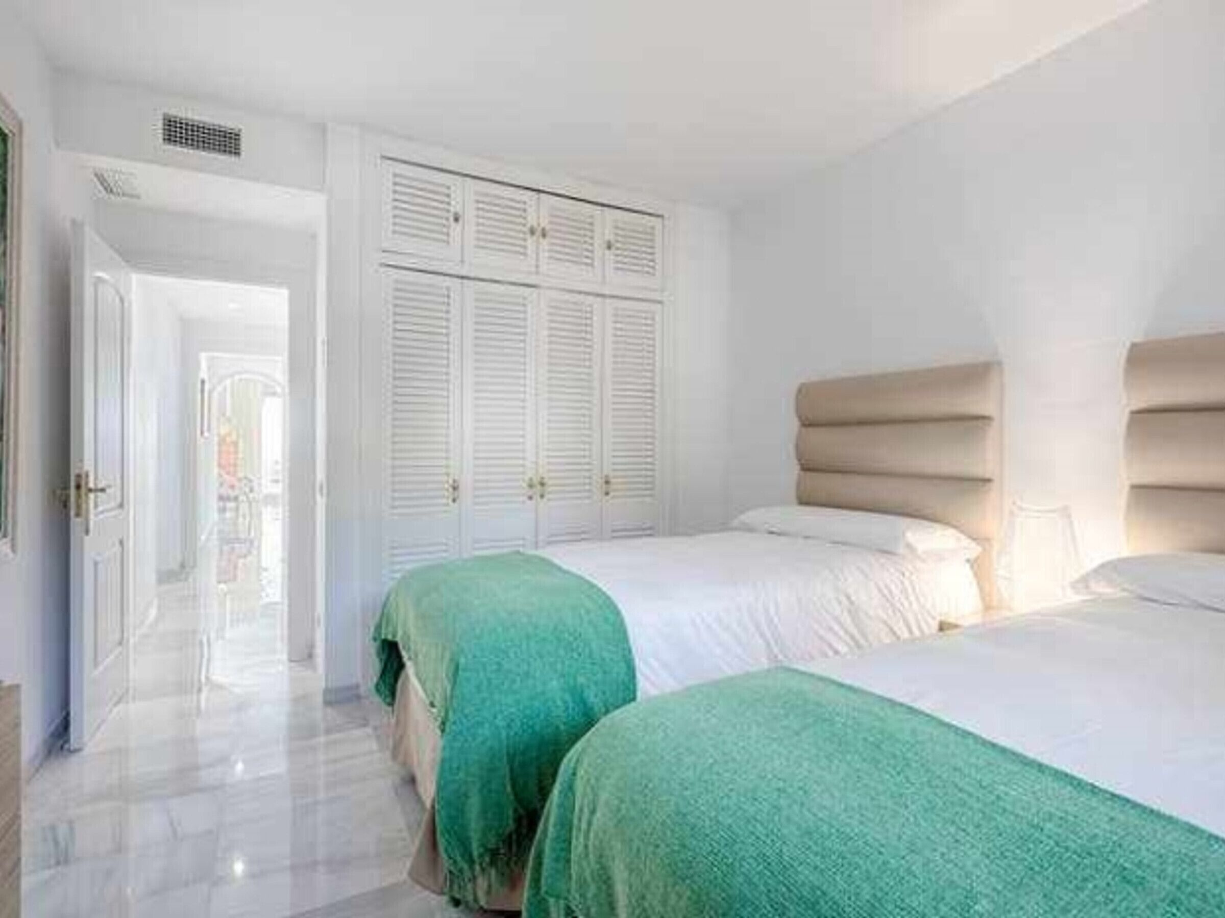A hotel room with two beds, a wardrobe, and a door leading to a corridor.