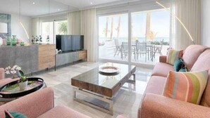 A modern living room with a sofa, coffee table, TV, and a balcony with outdoor furniture. - Luxury beachfront apartment with pool, gardens, tennis courts and restaurant in Estepona (Estepona)
