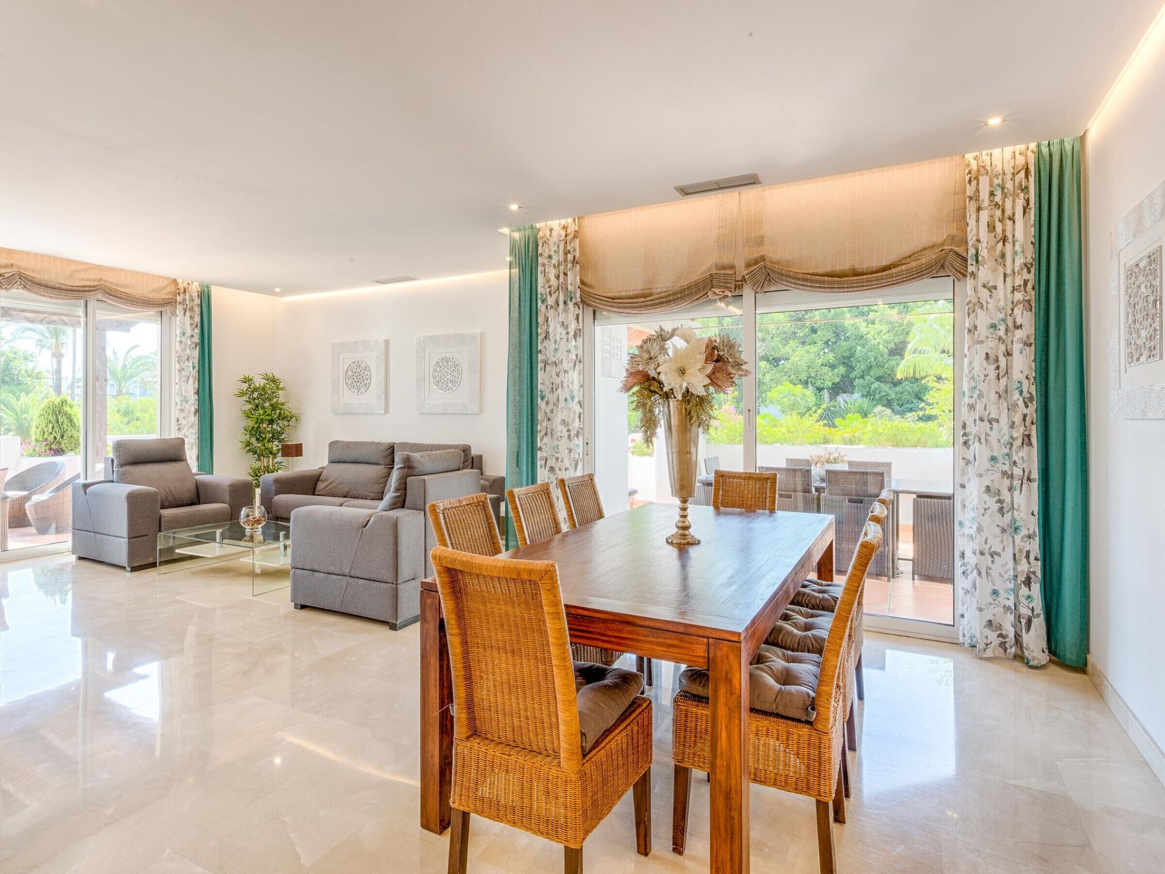 A spacious living room with a dining area, large windows, and a view of greenery outside.