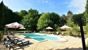 Piscina con sillas de descanso y sombrillas, rodeada de árboles.