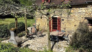 Una casa de piedra con patio empedrado, contraventanas rojas y chimenea de piedra.