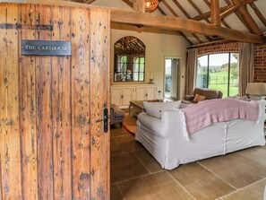 A rustic interior with a wooden door labeled "THE CARTHOUSE," a white sofa, and a large window offering a view of the outdoors. - The Carthouse (Ledbury)