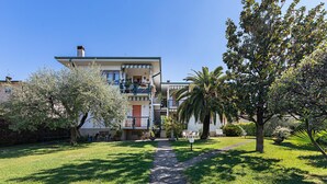 Un edificio residencial de varios pisos con una entrada central, rodeado de céspedes y árboles bien cuidados.