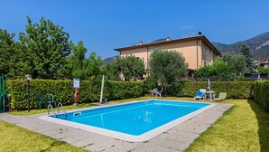 Piscina rectangular con borde blanco, rodeada por un césped cuidado y un seto.