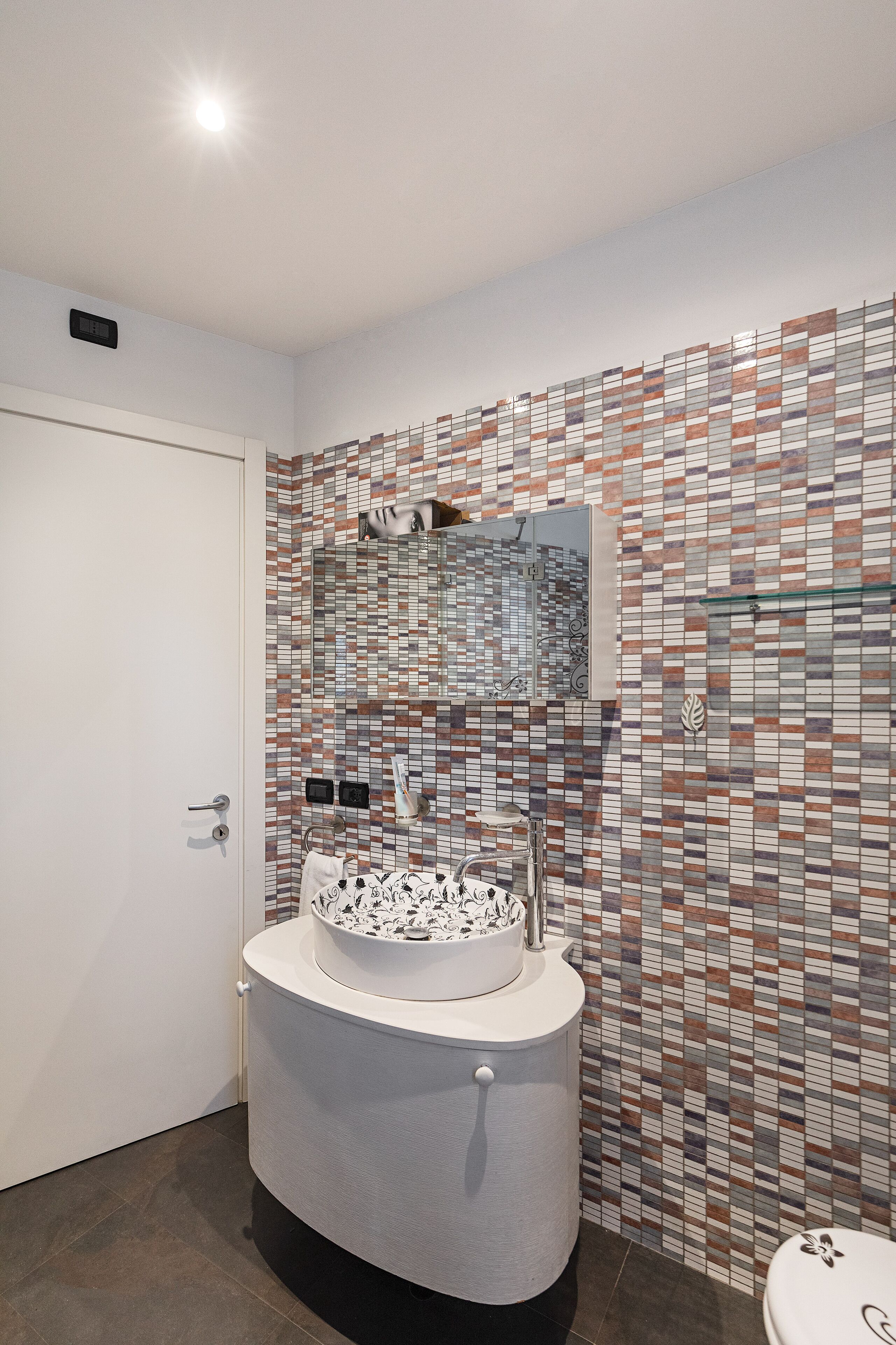 A bathroom with a tiled wall, a sink with a mirror, and a toilet.