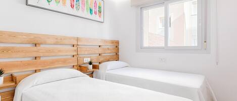 A hotel room with two beds, a wooden headboard, a window, and a colorful feather artwork on the wall.