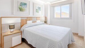 Un dormitorio con cama, mesitas de noche, una ventana con vistas y cuadros en la pared.