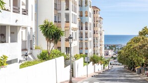 Una calle costera flanqueada por edificios de varios pisos, con balcones y una vista despejada del mar.