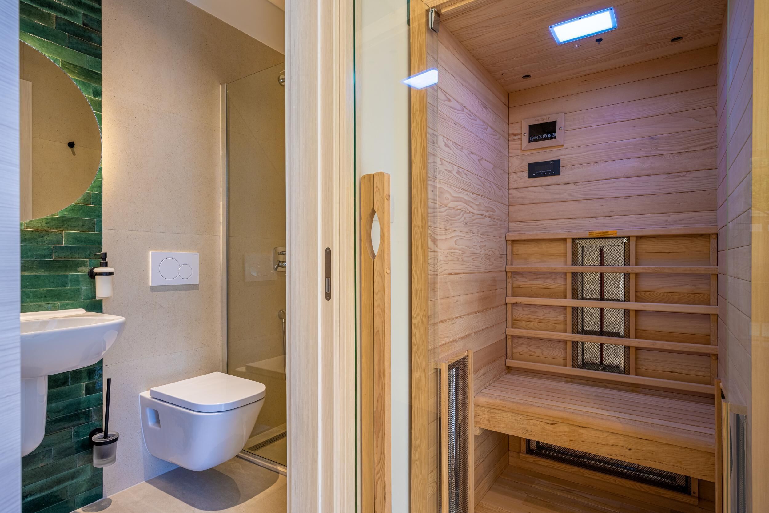 A modern bathroom with a glass shower enclosure, a white toilet, and a wooden sauna area with shelves.