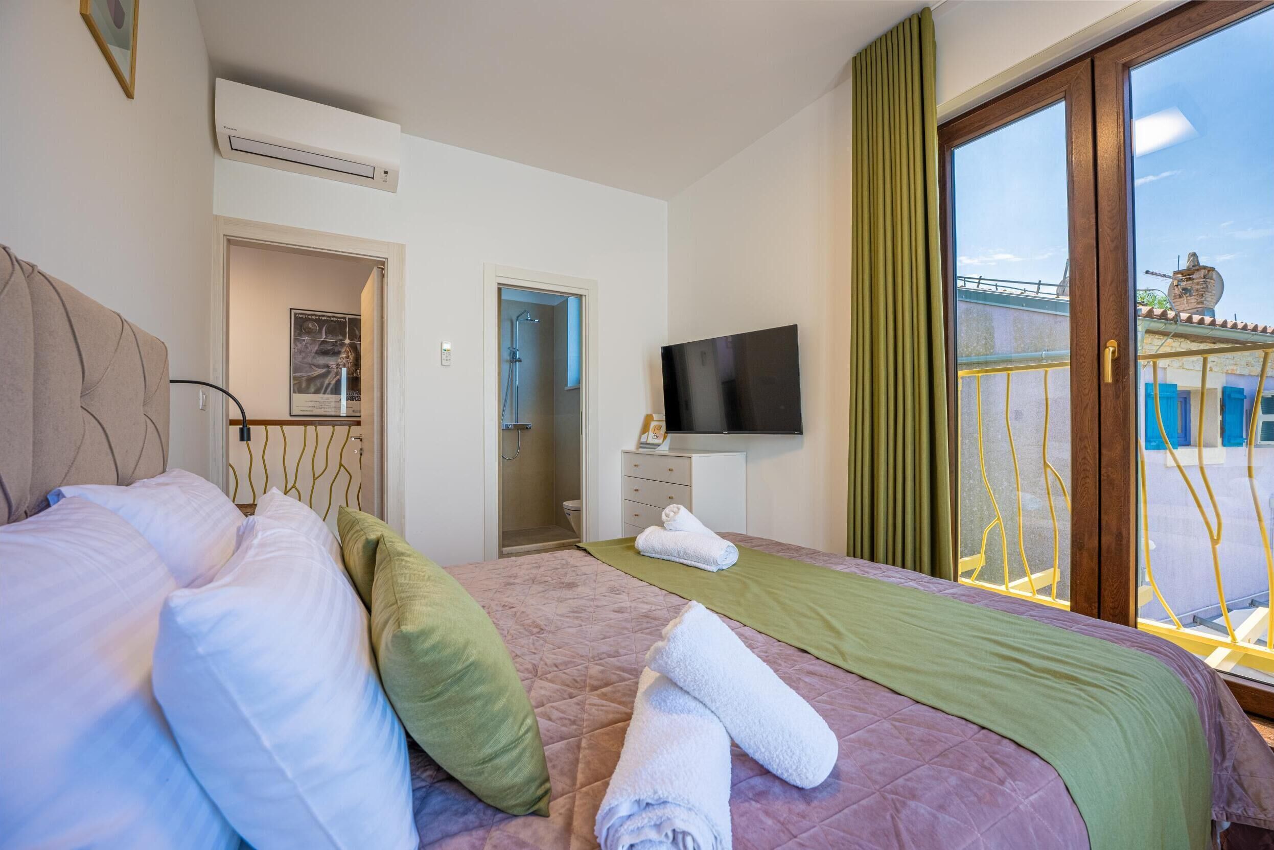 A hotel room with a bed, a TV, a bathroom, and a balcony with a view.